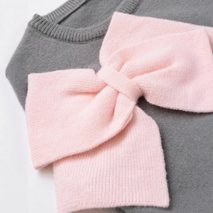 Grey knit top featuring a large contrasting pink bow decoration and ribbed textures