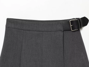 Détail d'un pantalon gris foncé avec texture lisse et ceinture en cuir noir à boucle argentée