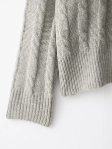 Gros plan sur la maille torsadée grise montrant les fibres de laine et les poignets côtelés