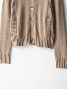 Close-up of brown knit cardigan featuring round buttons, patch pockets, and ribbed hem detail