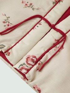 Close-up of printed kimono jacket with floral cross-stitch pattern and red tie closure