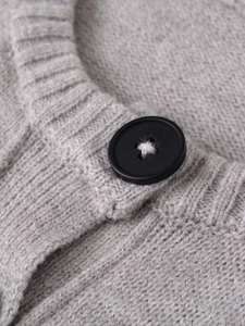 Close-up of a black button on light grey rib-knit soft long sleeve cardigan sweater