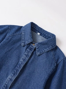 Detail of blue denim shirt collar featuring amber button and fine stitching texture