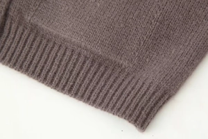 Gros plan des poignets côtelés du gilet en maille taupe montrant la texture douce