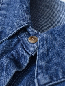 Detail of vintage blue denim shirt showing a classic collar and a brown resin button