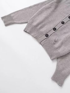 Detail of grey knit cardigan with black buttons and ribbed cuffs on white background