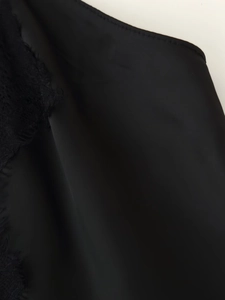 Close-up of smooth black satin fabric and delicate lace trim detail on the dress