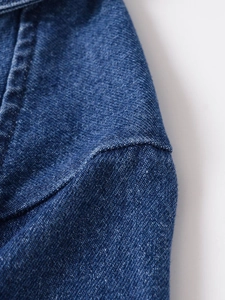 Macro view of blue denim fabric texture and reinforced stitching on shirt shoulder