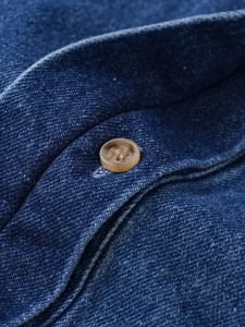 Close-up of blue denim fabric texture and brown resin button on long sleeve shirt