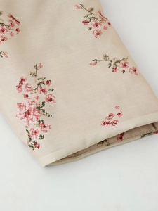 Macro detail of beige kimono coat fabric with pink and green pixelated floral embroidery