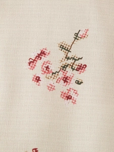 Macro detail of vintage floral cross-stitch embroidery on breathable beige cotton fabric