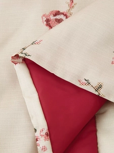 Close-up of kimono jacket hem featuring beige linen texture and red cross-stitch floral detail