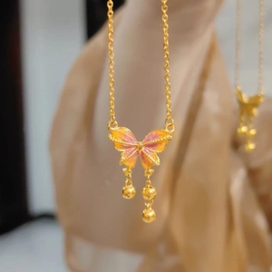 Close-up of golden butterfly pendant with gradient enamel and dangling small beads