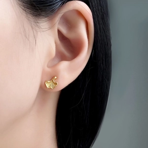 Detail of matte gold ginkgo leaf stud earring with fine radial texture on earlobe