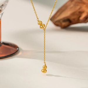 Detailed view of a gold-plated titanium steel Y-necklace with two polished hulu pendants
