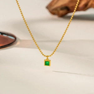 Detailed close-up of golden ball chain necklace with square emerald green gemstone pendant