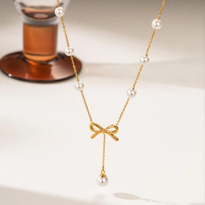 Macro detail of gold bow necklace with white pearls on a minimalist white background