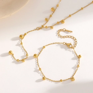 Detailed view of elegant gold beaded necklace and bracelet set on a white surface