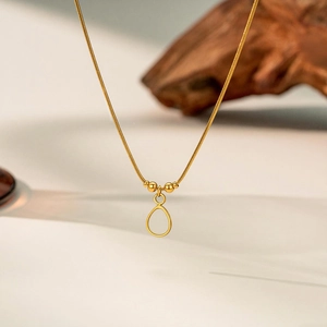 Macro shot of gold snake chain necklace with hollow teardrop pendant and gold beads