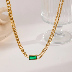 Detail of gold asymmetric chain necklace featuring a rectangular green gemstone pendant