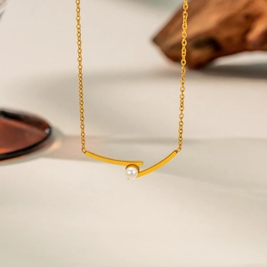 Macro shot of gold titanium necklace featuring a minimalist pendant with a white pearl