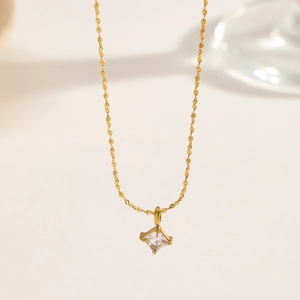 Macro shot of gold necklace with square claw-set zircon pendant on minimalist background