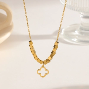 Elegant gold clover necklace with hollow pendant and hexagonal beads on warm background