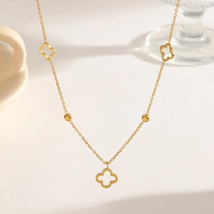 Elegant gold hollow clover titanium necklace with delicate beads on beige background