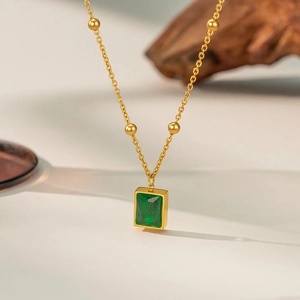 Close-up of gold titanium necklace with emerald-cut green stone and bead chain