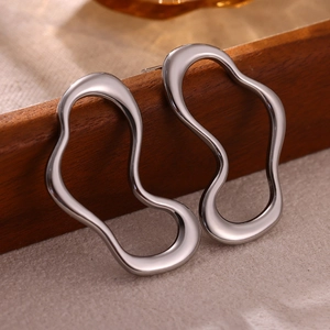 Macro shot of silver irregular wavy earrings showing mirror-like metallic luster on wood
