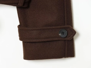 Close-up of dark brown wool jacket cuff featuring a decorative strap and marbled button