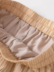 Detailed macro view of the elastic waistband and fine accordion pleats on beige wide leg pants
