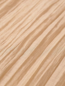 Macro shot of apricot translucent pleated wide-leg trousers showing fine mesh texture
