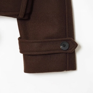 Deep brown wool jacket sleeve detail featuring decorative cuff straps and precise stitching