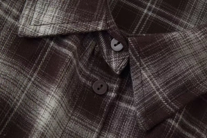 Detailaufnahme des spitzen Kragens und der Knöpfe eines braun karierten Flanellhemds