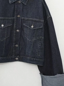 Gros plan sur une veste en jean noire avec surpiqûres blanches et poignets retroussés