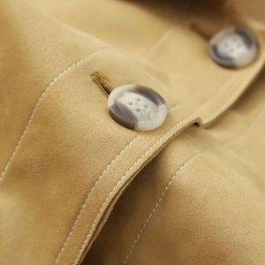 Detail of mustard yellow suede jacket featuring marble texture button and white stitching