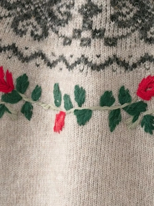 Detailed view of Fair Isle pattern and red floral embroidery on beige knitted sweater