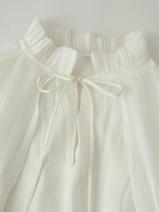 Detail of white ruffled high neck dress with delicate ribbon tie and pleated chiffon texture