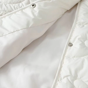 Detail of white quilted jacket showing round metal snap buttons and fine stitching texture