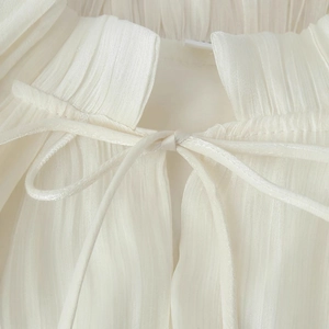 Close-up of a white ruffled long dress with drawstring neckline and pleated fabric details