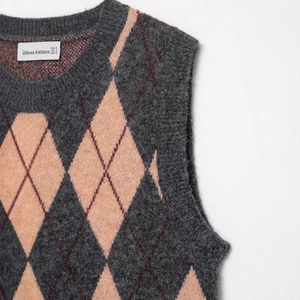 Primer plano de chaleco de punto de rombos rosa y gris con cuello redondo y textura suave