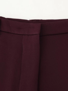 Detailed view of dark burgundy trousers waistline featuring belt loops and stitching