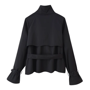 Detail of double-breasted black cropped trench coat with storm flap and belted waist