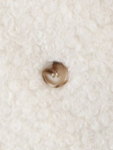 Dettaglio del tessuto boucle color crema con un bottone marmorizzato marrone sulla giacca