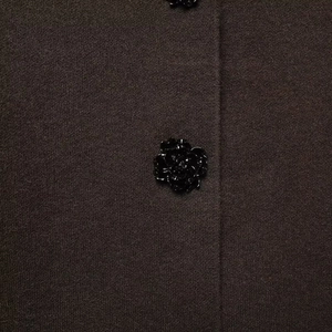 Macro detail of dark brown knit blazer featuring an elegant black 3D flower-shaped button