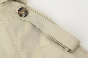 Detail of shoulder epaulet on beige double-breasted trench coat with tortoiseshell button