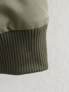 Gros plan détaillé des poignets côtelés de la veste d'aviateur en patchwork vert olive