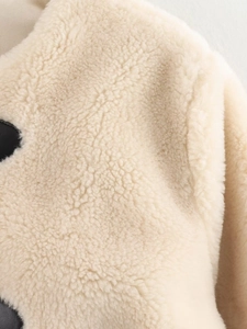 Close-up of thick off-white sherpa fleece fabric with high-density plush texture and black spots