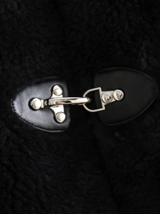 Macro detail of the silver metal clasp on black faux shearling coat fabric with leather base